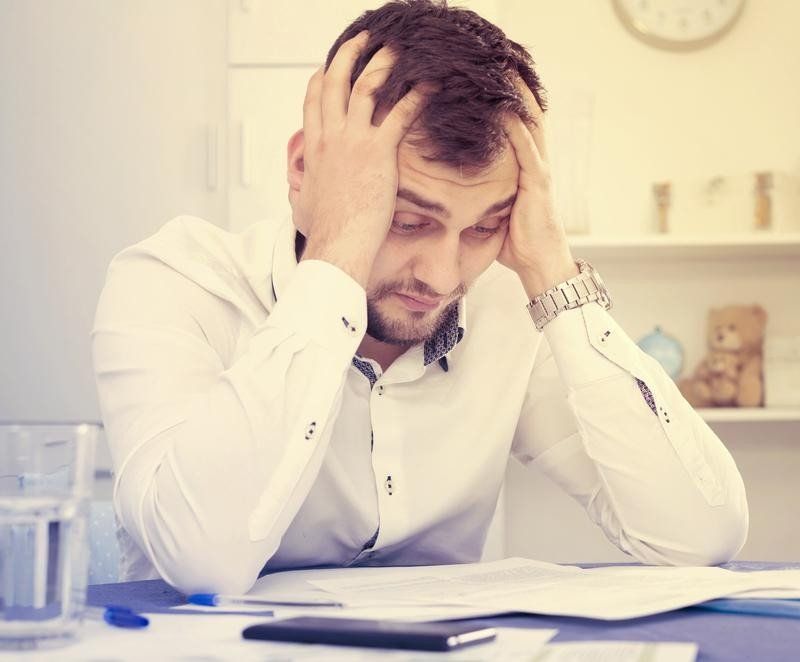 A man is sitting at a table with his hands on his head.